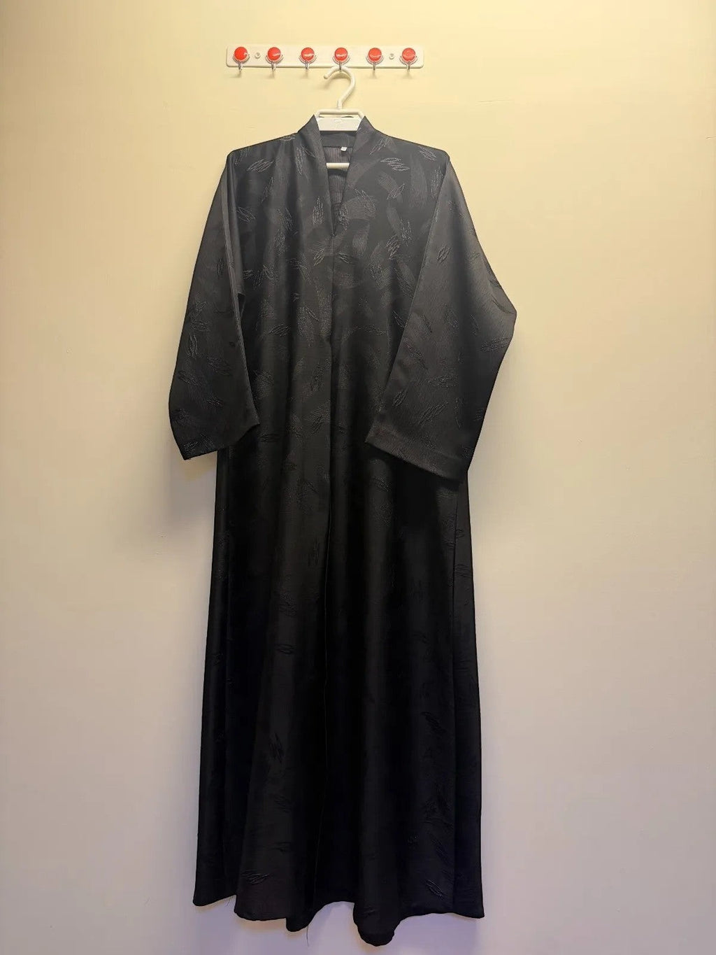 A&M FANCY STORE elegant black abaya with textured leaf pattern and V-neckline. Long sleeves, flowing silhouette.