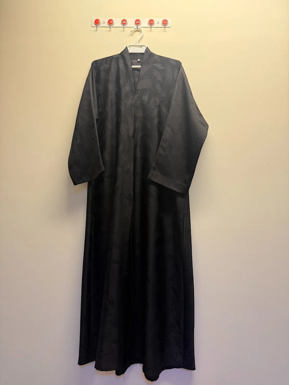 A&M FANCY STORE elegant black abaya with textured leaf pattern and V-neckline. Long sleeves, flowing silhouette.